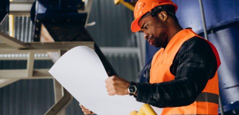 African american worker standing in uniform wearing a safety hat in a factory