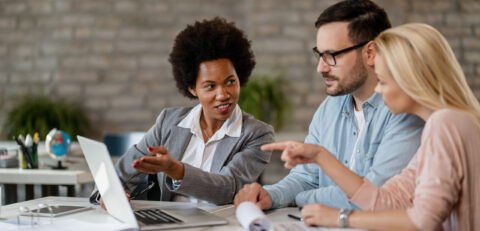 Black female insurance agent using computer with a couple during consultations in the office.